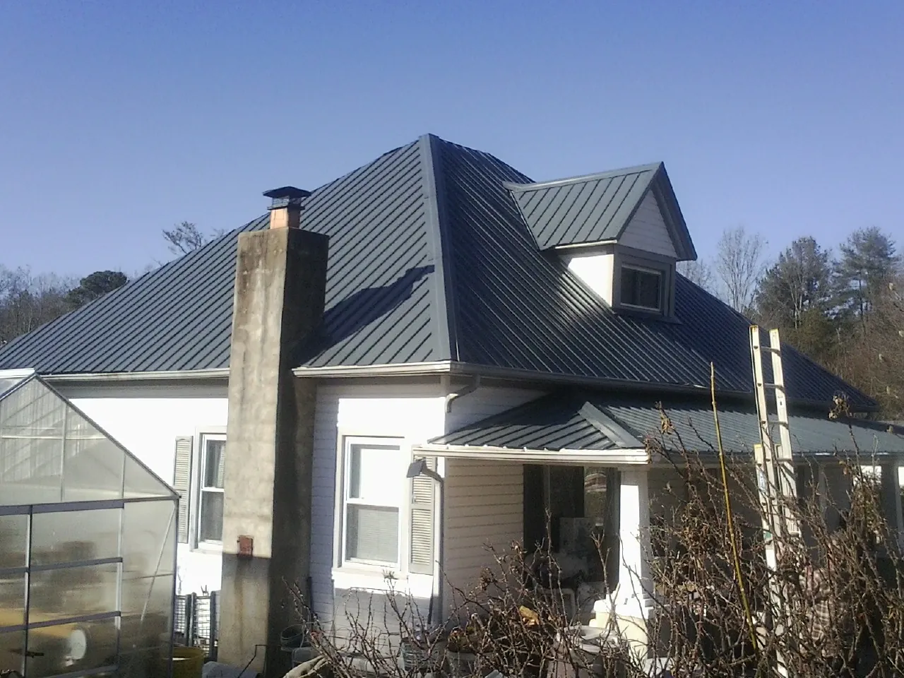 Dark blue standing seam metal roof on a white farmhouse with dormer — Slate & Tile Roof Repair by Roofing Brothers in Verden
