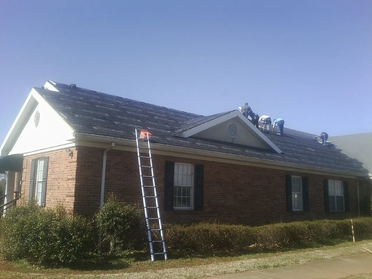 Crew tearing shingles off a brick ranch roof with a ladder set — Emergency Roof Repair work by our crew in Verden