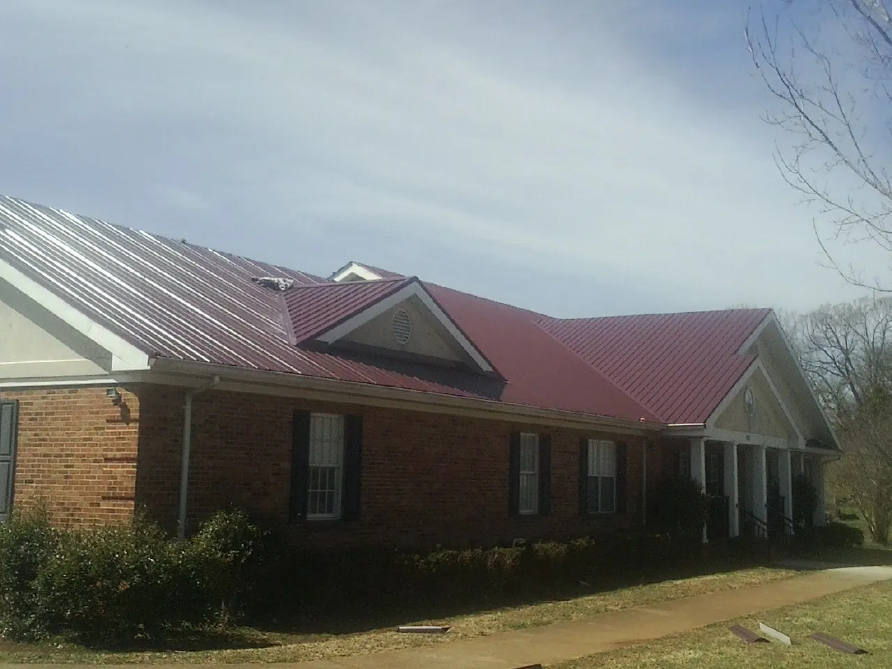 Red metal roof with gabled entries on a long brick building, from a Hail Damage Roof Repair job in Verden