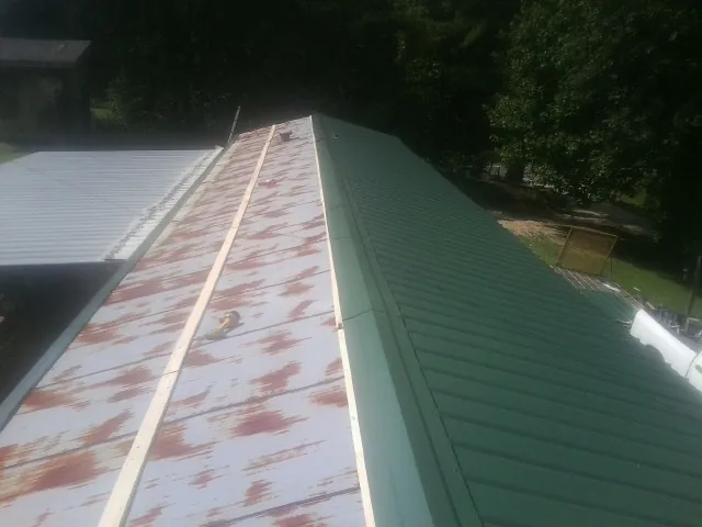 Old rusted panels beside newly installed green metal roofing — Wind Damage Roof Repair by Roofing Brothers in Verden