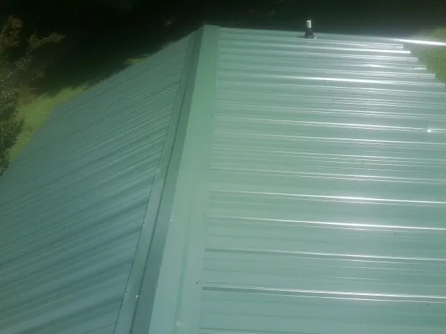 New green metal panels meeting at the ridge of a roof — Flat Roof Repair work by our crew in Verden