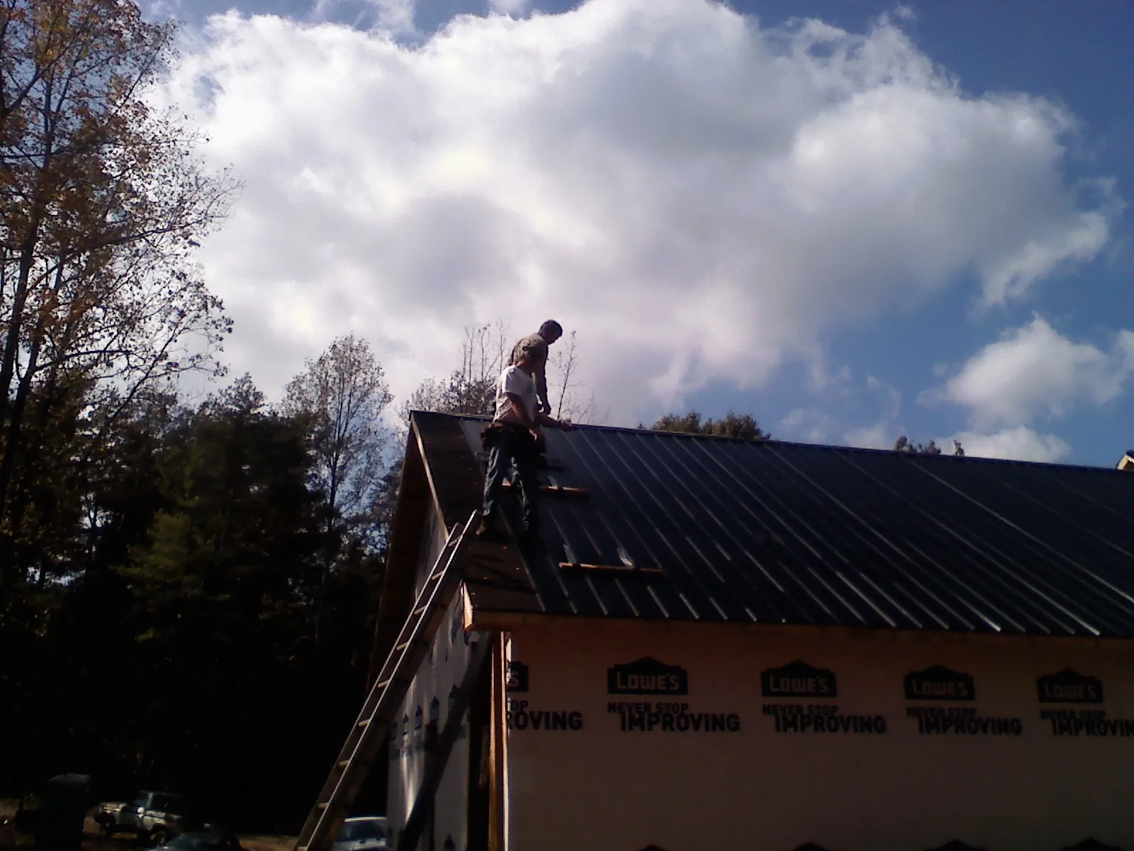 Roofer fastening dark metal panels high against a cloudy sky, from a Roof Inspection job in Verden