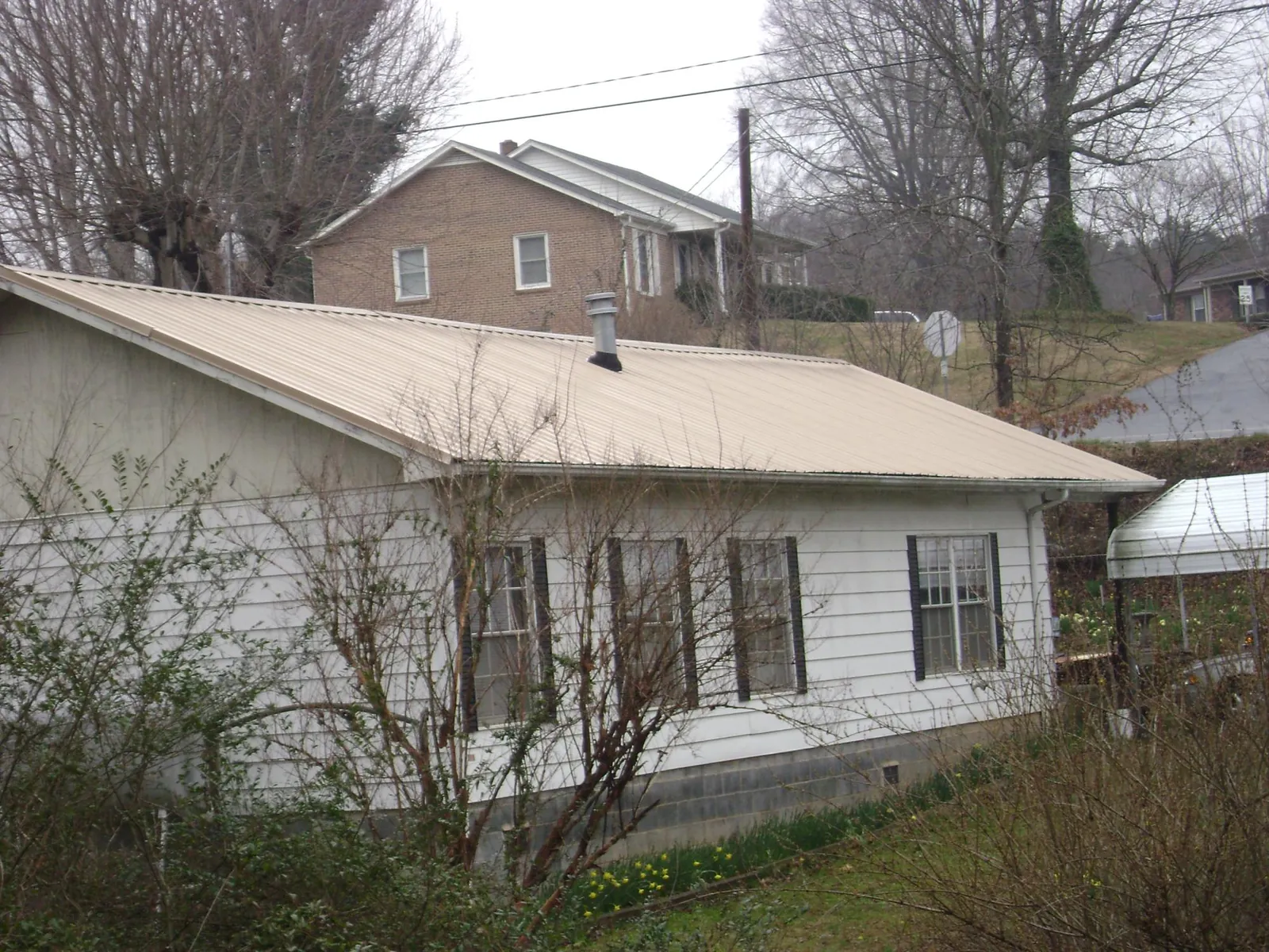 Tan metal roof on a white sided house set into a hillside — Commercial Roofing by Roofing Brothers in Verden